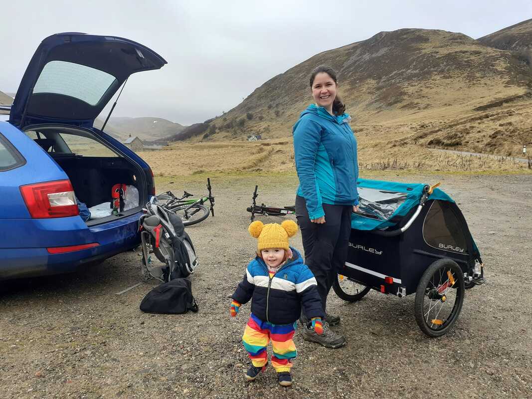 Getting ready to go. Cat is building the bike trailer. Maisie is dressed in rainbow waterproof dungarees and a warm hat
